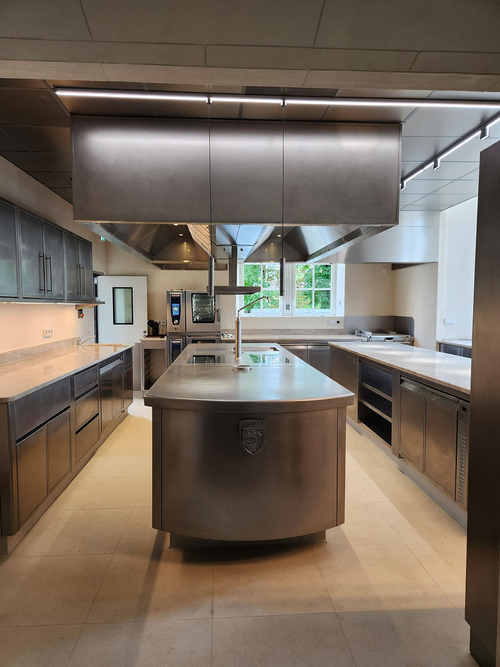 Cuisine professionnelle avec un grand îlot central, fourneaux, et équipements en acier inoxydable.