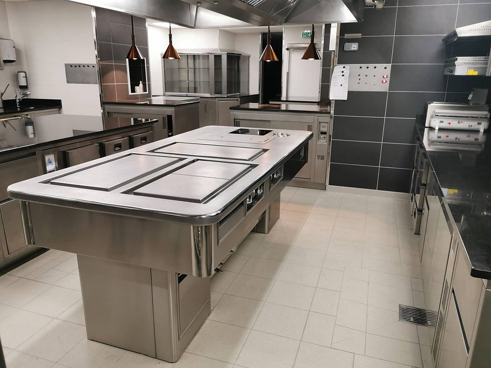Cuisine professionnelle avec un grand îlot central, fourneaux, et équipements en acier inoxydable.