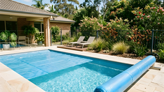 Backyard pool half covered by a blue bubble solar pool blanket, with the rest rolled onto a cover roller at the edge