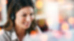 A woman wearing a headset smiling at a computer screen