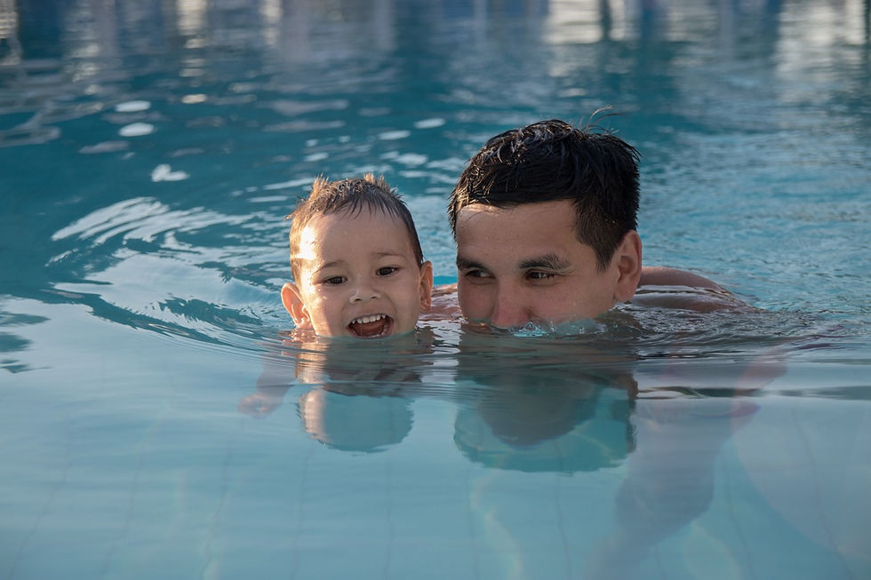 Man and young child smiling with heads above water in a blue swimming pool, sharing a playful swim.