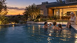 Family relaxing in a heated backyard pool at dusk with the Adelaide skyline behind