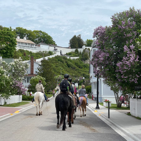 Horseback riders on a lilac tree lined street with Fort Mackinac in the background