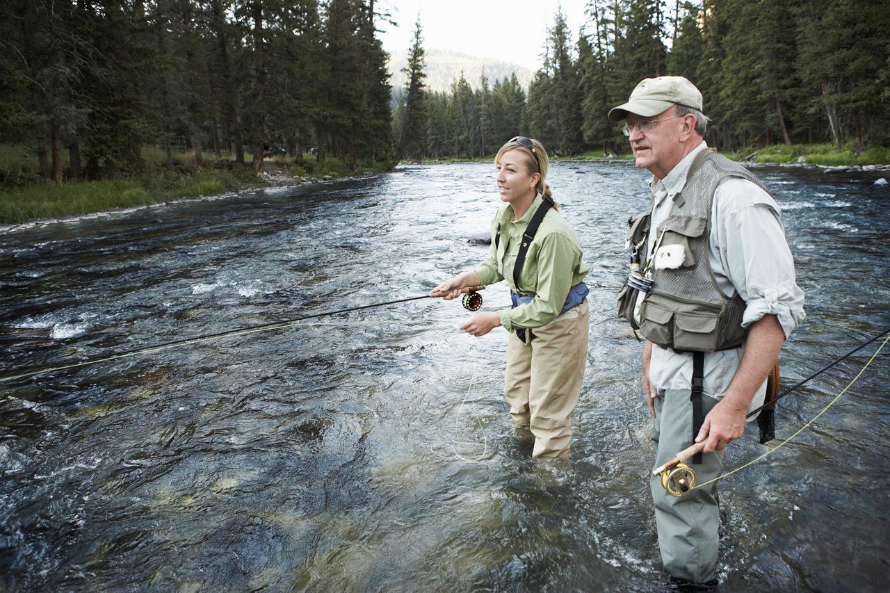 father and daughter having a trout fishing experience in a wooded river together