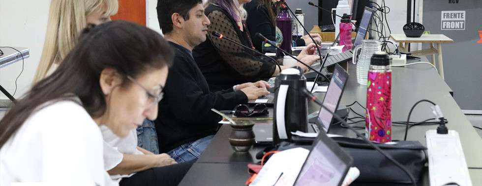 Reunión de Consejo de Unidad.  Grupo de personas sentadas detrás de una mesa alargada, cada una con un micrófono delante y una notebook.