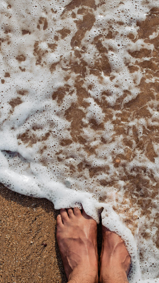 Ocean waves washing over feet on a sandy beach, symbolizing coastal living and everyday exposure to sea salt