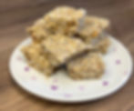 Granola bars stacked on a plate with pink heart patterns, set on a wooden table. The bars are made of oats and seeds, creating a rustic vibe.