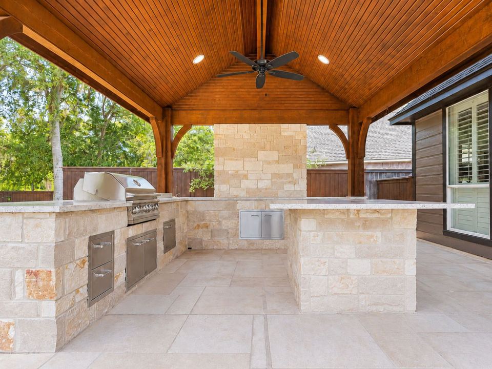 Newly completed covered outdoor kitchen with stone counters, built-in grill, wood ceiling, and open patio layout.