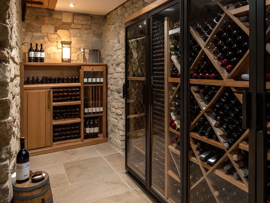 Custom home wine cellar with stone walls, wood wine racks, glass doors, and warm lighting.