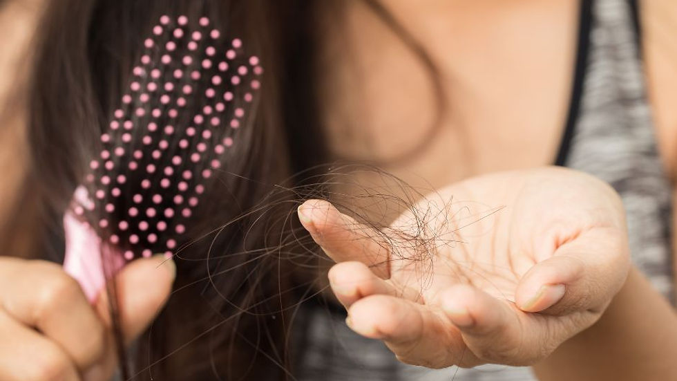 A woman holding a pink hair brush in front of her with her other hand out showing hair loss