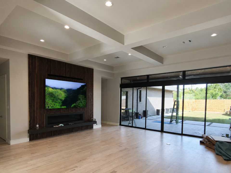 Living room remodel with custom wood slat fireplace wall, mounted TV, light wood flooring, recessed ceiling details, and large sliding glass doors.