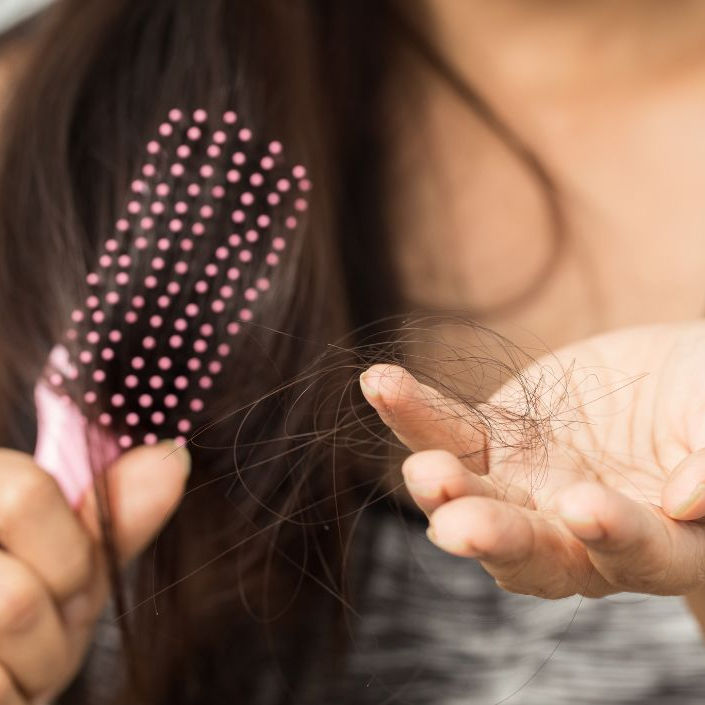 A woman holding a pink hair brush in front of her with her other hand out showing hair loss