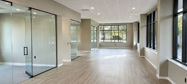 Completed commercial interior update with modern glass offices, polished floors, and finished ceiling panels.