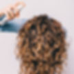 Woman with long curly hair spraying product with her hair flipped over