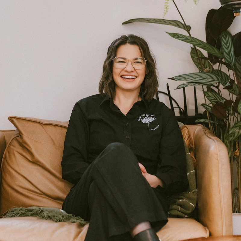 Woman smiling with shoulder-length brown hair wearing a black uniform sitting on a couch on a brown couch