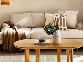 Bright beige living room with sofa, wooden coffee table, plant vase, lamp, and sunlit rug; calm, cozy, minimalist decor
