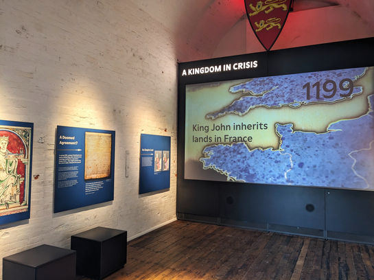 Audio visual against wall showing the map between France and England dated 1199. Interpretation panels featuring images and text.