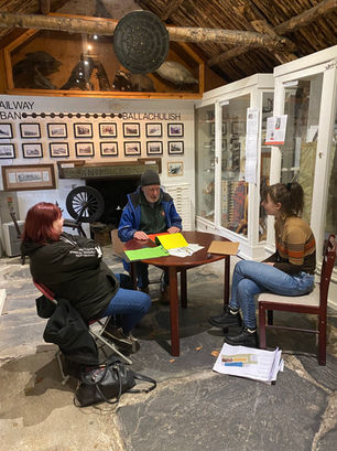 Three people in a cottage, sat around a table talking.