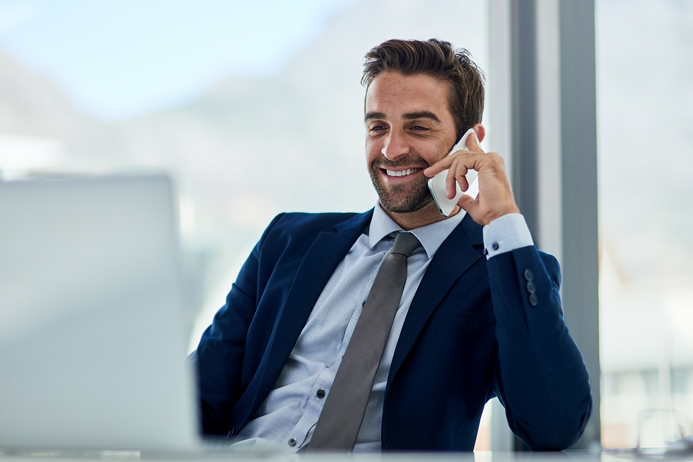 Homem de terno sorrindo enquanto fala ao telefone em frente ao notebook, passando uma imagem de confiança e domínio da gestão condominial, representando um síndico experiente.