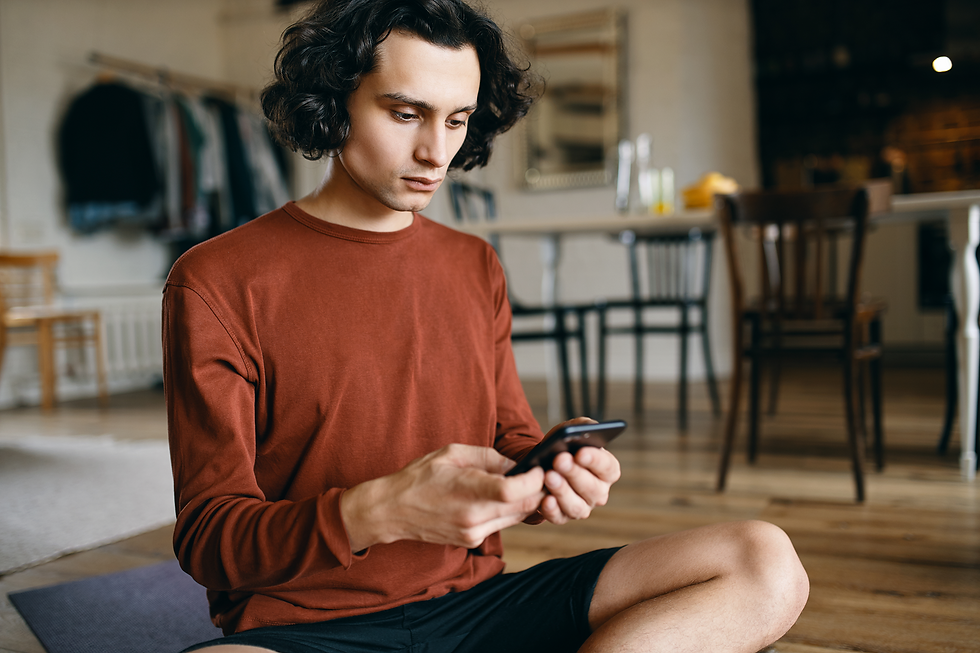 Homem jovem sentado em casa, olhando para o celular com expressão séria, representando o uso do WhatsApp como prova em situações de condomínio.