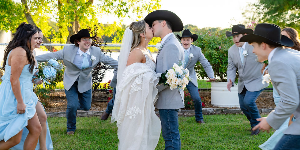 Bride and groom kiss outdoors while bridesmaids and groomsmen in cowboy hats cheer, holding blue and white bouquets at a wedding venue near Rosenberg Texas that can hold up to 200 people