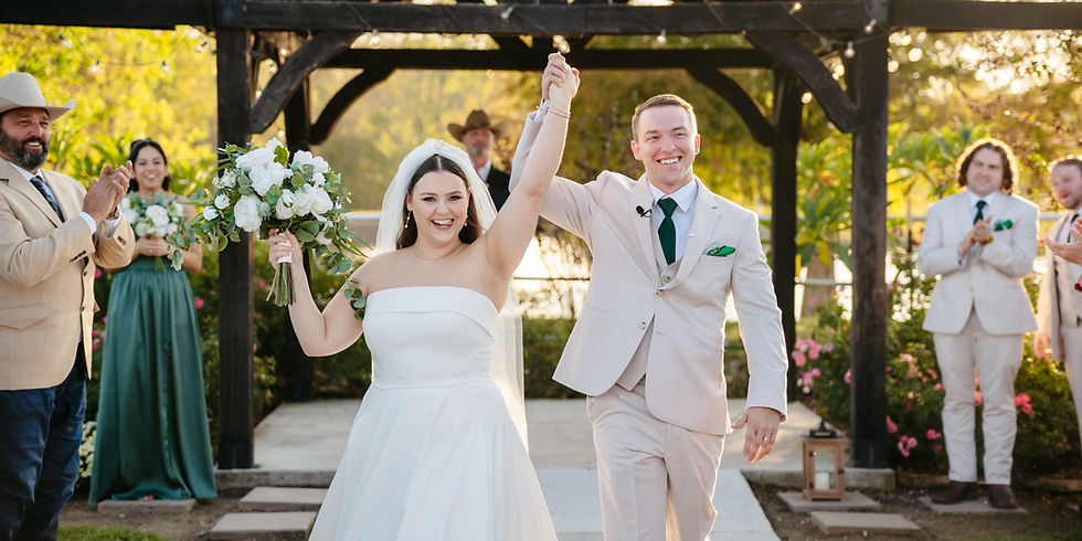Bride and groom in beige suit raise hands and smile after outdoor wedding ceremony, guests applaud under a pergola at a wedding venue that can hold 170 people near Houston, Texas.