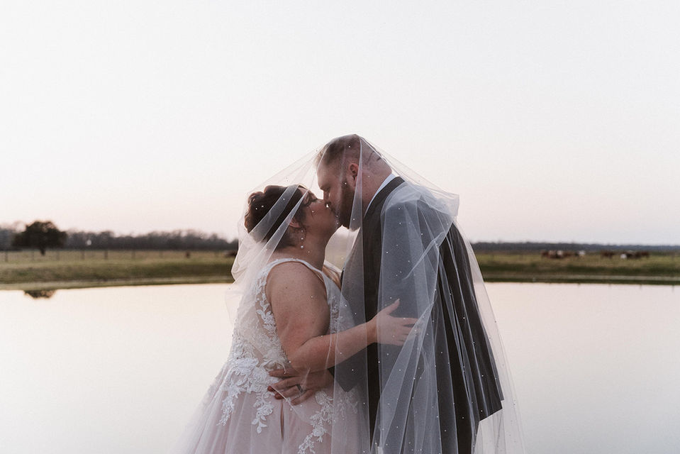 Newlywed couple kissing on dock with pond background at wedding venue that holds up to 200 guests near Sugar Land, Texas