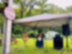 Charity Gilbert, the Community Aid Coordinator, enchants the farmers market with a lively banjo performance under a cozy canopy.