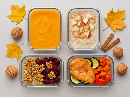 Őszi ízletes meal prep dobozok felülnézetből: sütőtökkrémleves, almás-fahéjas zabkása, cékla-quinoa saláta dióval és sült csirkemell zöldségekkel, körül őszi levelek, diók és fahéjrúd.