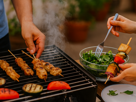 Két ember grillezik együtt nyári környezetben – az egyik csirkemellnyársakat forgat a rácson, a másik friss salátát készít tofu- és zöldségnyárssal a kezében. Gőzölgő grill, színes alapanyagok és barátságos, kerti hangulat.