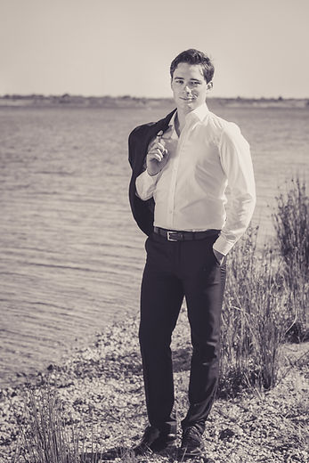 Robert Pohlers steht an einem See, das Jacket über eine schulter geworfen und schaut in die Kamera. Das Bild ist schwarz-weiß.