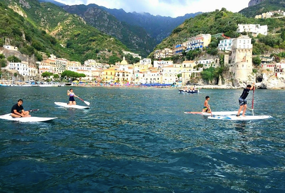 People paddleboarding on the water with a scenic coastal town background Sup Club Positano