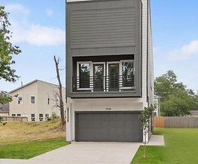Modern three-story home with a gray and white exterior, two-car garage, and private second-floor balcony with black railing; concrete driveway and green lawn on both sides, with wood privacy fencing and neighboring homes visible in the background.