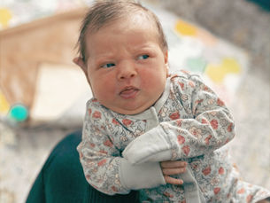 A small infant wearing blue patterned pajamas makes a skeptical face