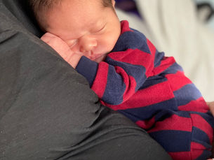 A newborn baby in red and blue pajamas rests on a chest in a black shirt