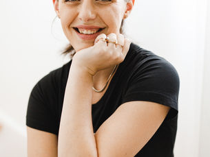 A woman sits on stairs with against a white wall. Her hand rests under her chin.