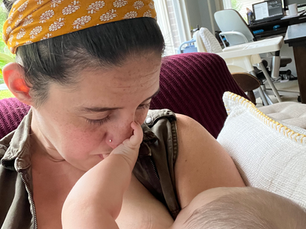 A woman with brown hair breastfeeds a baby who is playing with her nose