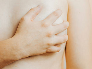 A woman grips her left breast with her right hand