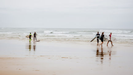 Surfers walking towards the ocean on a cloudy day.