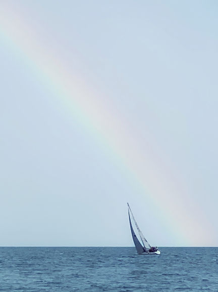 Sailboat on the ocean beneath a rainbow.