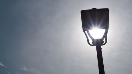 Streetlight shining brightly against a gray sky.