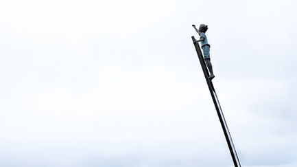 Child climbing a tall ladder against the sky.