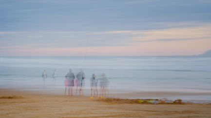 Blurred figures walking on a beach at sunset.