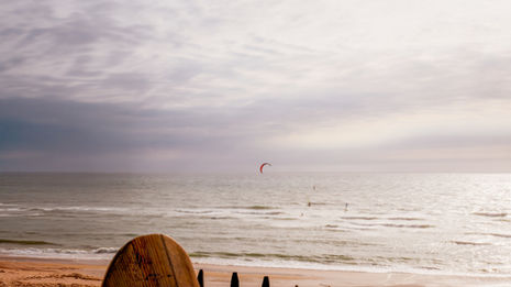 Surfboard on beach, ocean waves, cloudy sky.
