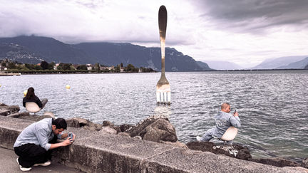Giant fork sculpture near a lakeside with mountains.