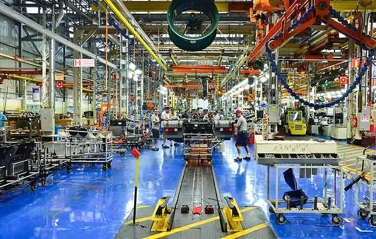 Linha de montagem de fábrica de carros com operários, máquinas e esteiras; chão azul e estrutura industrial movimentada.