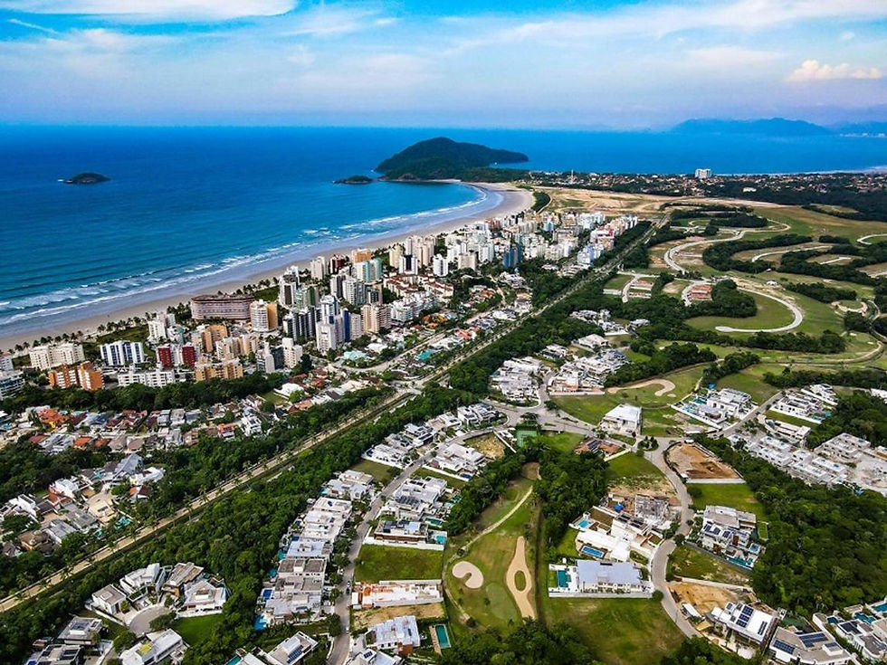 Vista aérea de cidade costeira com praia azul, arranha-céus, campo de golfe e ilhas ao fundo sob céu claro.