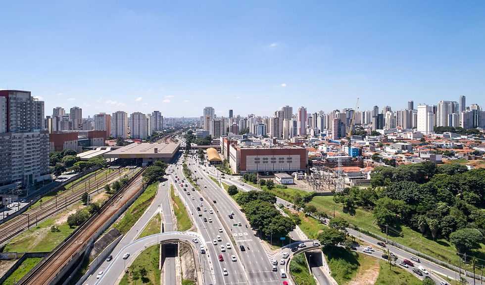 Vista aérea de avenida movimentada com carros, trilhos de trem e arranha-céus sob céu azul.