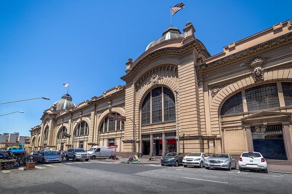 Mercado Municipal histórico com cúpulas, bandeira ao vento e carros estacionados sob céu azul.