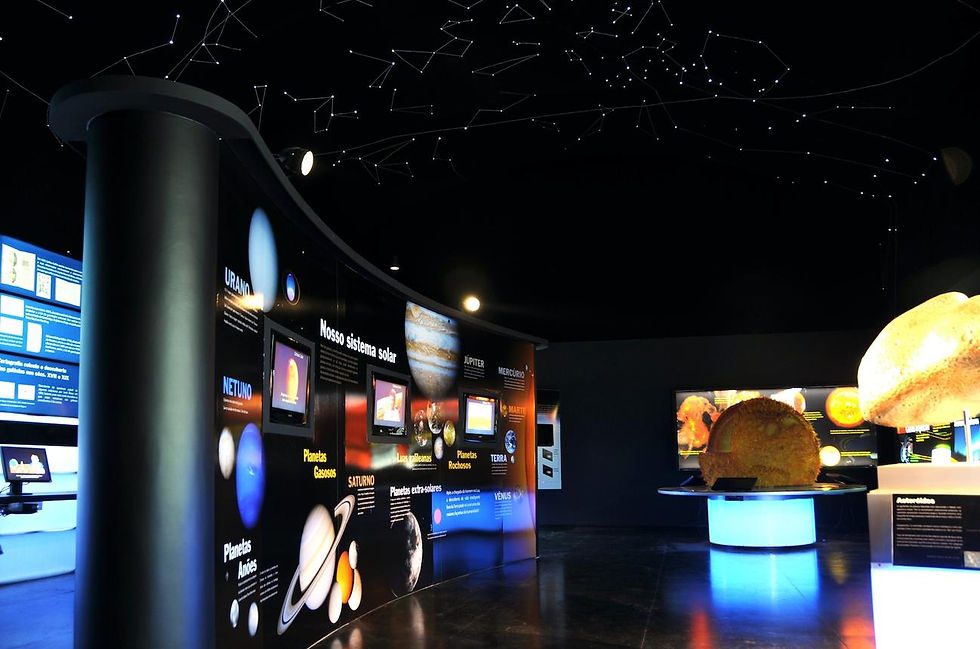 Museu escuro com exposição de astronomia: painéis de Nosso sistema solar, planetas iluminados e teto com estrelas.